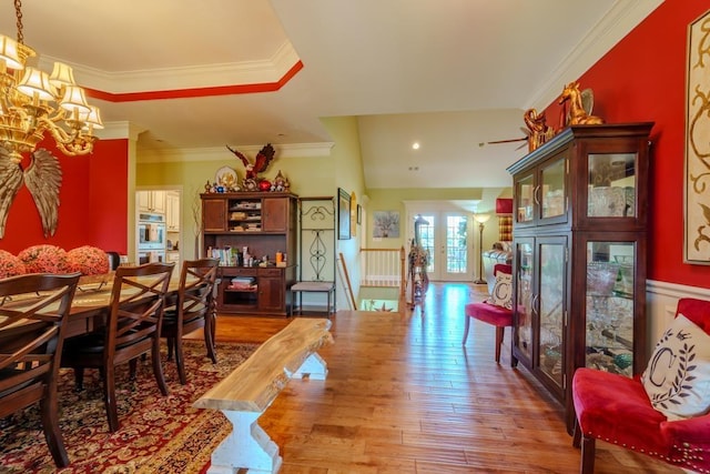 dining space featuring french doors, light wood-type flooring, a tray ceiling, crown molding, and an inviting chandelier