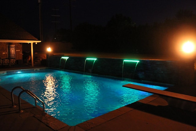 pool at night with a fenced in pool and a diving board