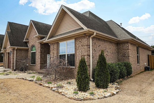 view of home's exterior featuring an attached garage, brick siding, and roof with shingles