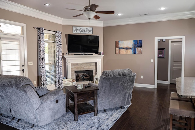 living area featuring a stone fireplace, crown molding, baseboards, ceiling fan, and dark wood-style flooring