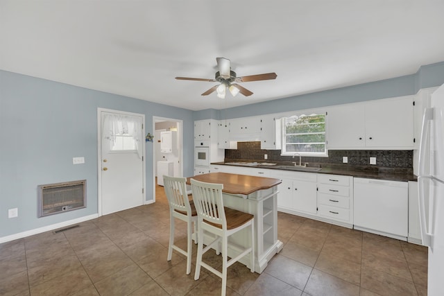  - kitchen featuring white appliances, a sink, dark countertops, heating unit, and tasteful backsplash