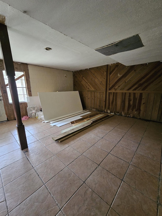 bonus room featuring light tile patterned floors, wooden walls, and a textured ceiling