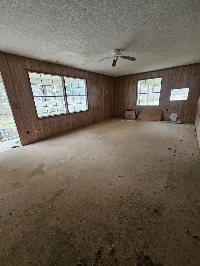 unfurnished room with wood walls, a textured ceiling, and a wealth of natural light