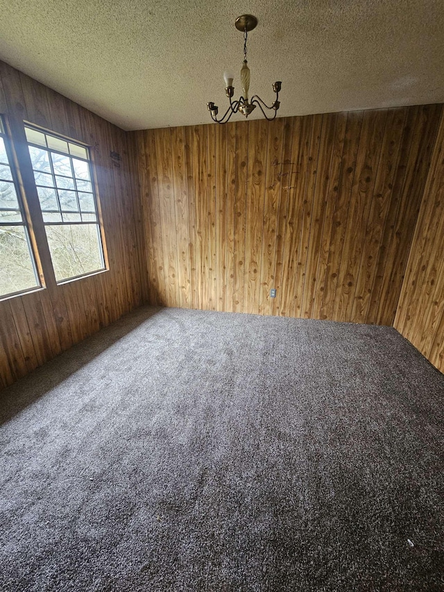 unfurnished dining area featuring an inviting chandelier, wood walls, a textured ceiling, and carpet flooring