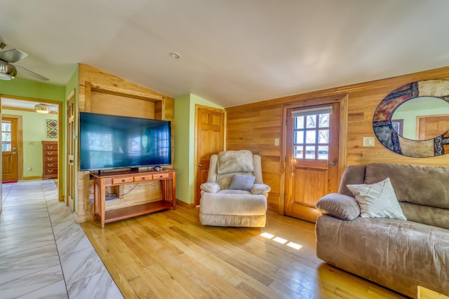 living room featuring light wood-type flooring, vaulted ceiling, ceiling fan, and wooden walls