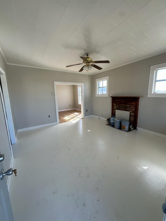 unfurnished living room with crown molding, a ceiling fan, a brick fireplace, concrete flooring, and baseboards