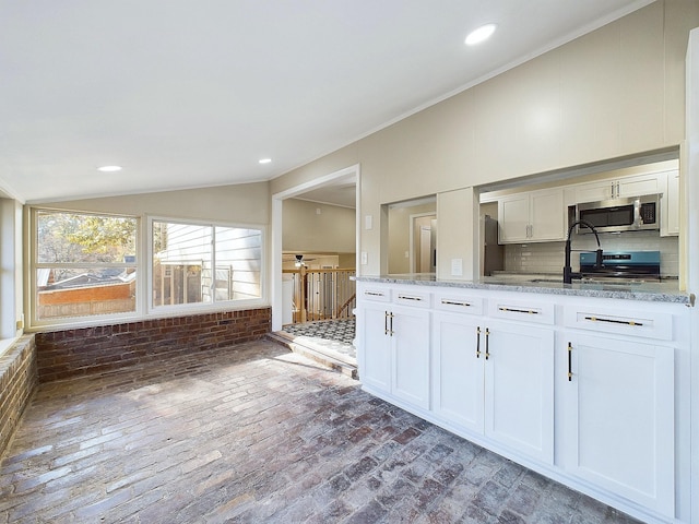 kitchen with white cabinetry, sink, light stone countertops, vaulted ceiling, and decorative backsplash