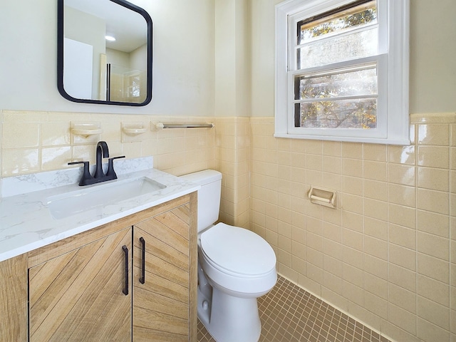 bathroom with toilet, vanity, tile patterned floors, and tile walls