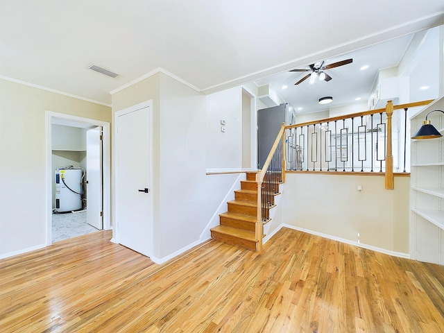 stairway featuring hardwood / wood-style floors, ceiling fan, ornamental molding, and water heater