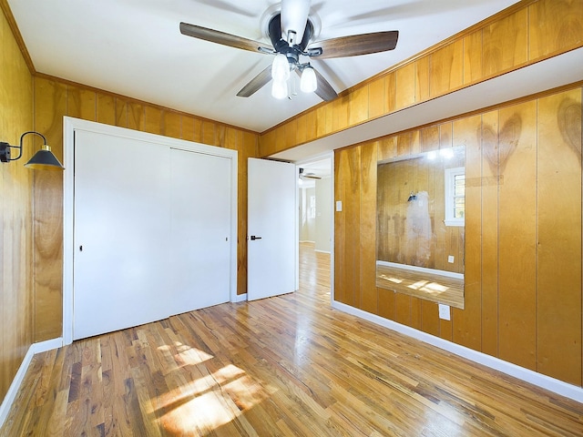 unfurnished bedroom featuring hardwood / wood-style flooring, ceiling fan, wooden walls, and a closet