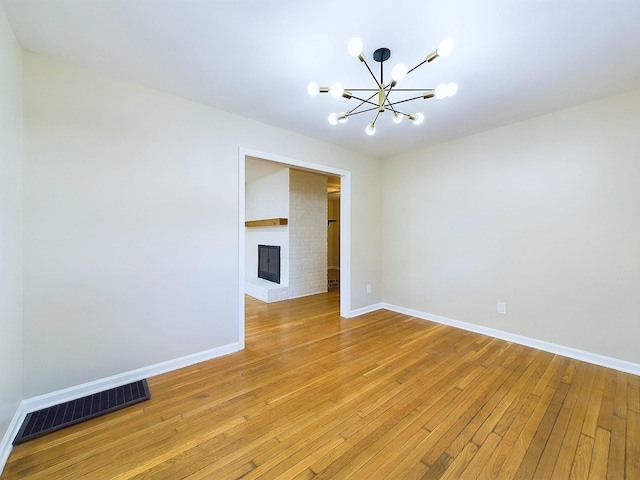 unfurnished room featuring a fireplace, light hardwood / wood-style flooring, and an inviting chandelier