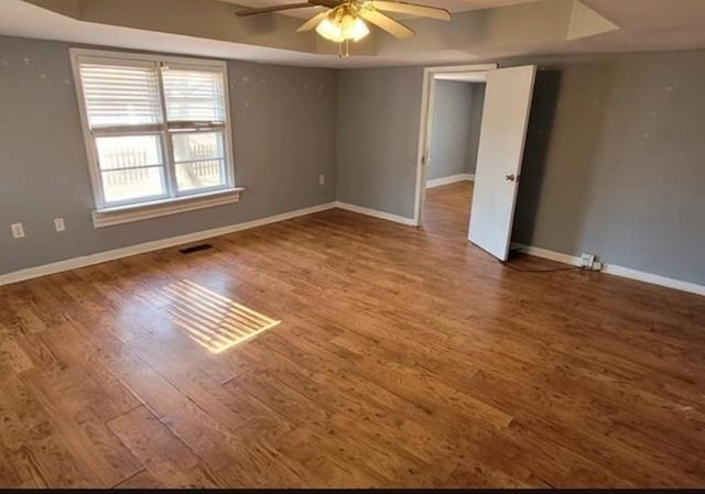 unfurnished room featuring a raised ceiling, ceiling fan, and wood-type flooring