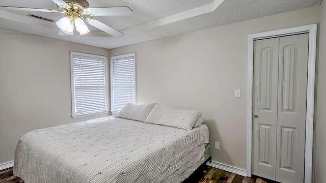 bedroom featuring dark wood-style floors, a closet, visible vents, a textured ceiling, and baseboards