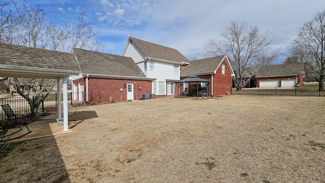 back of house with brick siding, fence, a gazebo, and roof with shingles