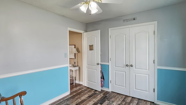 unfurnished bedroom with a textured ceiling, a ceiling fan, baseboards, a closet, and dark wood-style floors