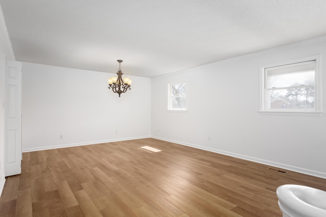 spare room with a chandelier, light wood-type flooring, visible vents, and baseboards