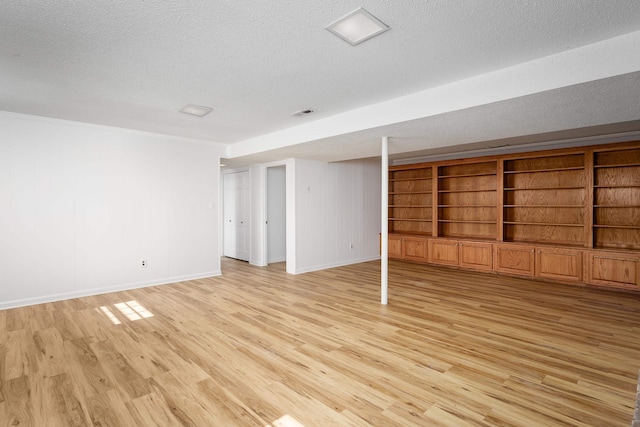 finished basement featuring built in shelves, baseboards, a textured ceiling, and light wood finished floors