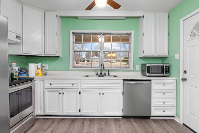 kitchen with sink, hardwood / wood-style flooring, stainless steel appliances, range hood, and white cabinets