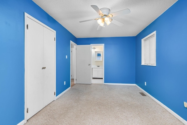 unfurnished bedroom with light colored carpet, ceiling fan, a textured ceiling, ensuite bath, and a closet