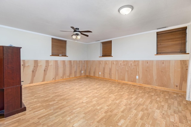 empty room featuring ornamental molding, wooden walls, ceiling fan, and light hardwood / wood-style flooring