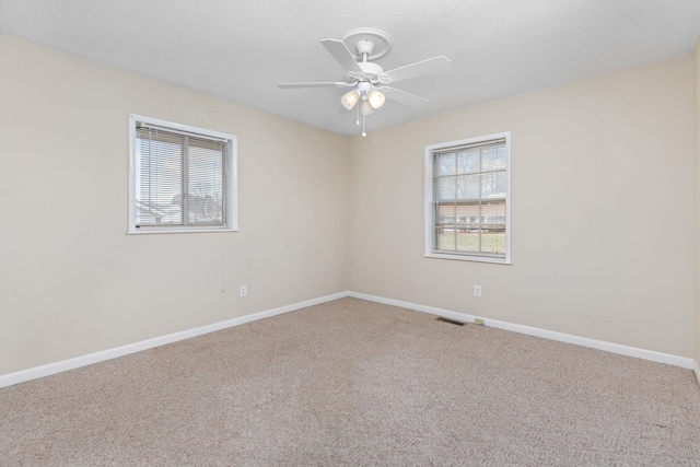 empty room with plenty of natural light, ceiling fan, and carpet