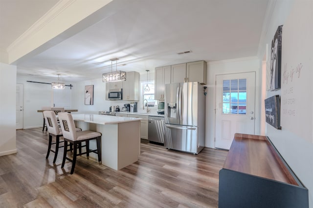 kitchen with appliances with stainless steel finishes, gray cabinetry, hardwood / wood-style floors, a kitchen island, and decorative light fixtures