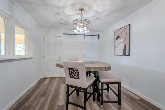 dining space with hardwood / wood-style flooring, ornamental molding, a barn door, and a chandelier