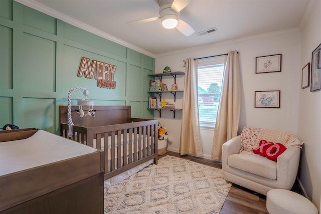 bedroom featuring ceiling fan, a crib, ornamental molding, and wood-type flooring