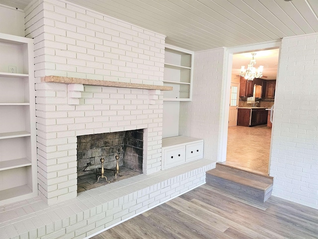  - unfurnished living room with a brick fireplace, a chandelier, built in shelves, wood finished floors, and wooden ceiling
