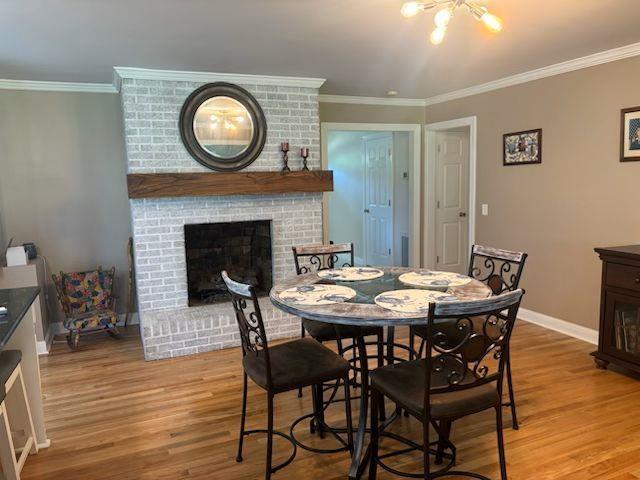  - dining area featuring light wood finished floors, crown molding, and a brick fireplace