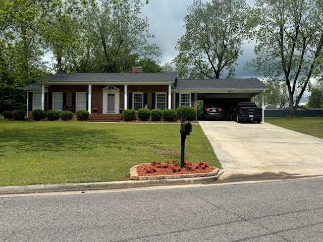 view of front of property featuring a chimney, an attached carport, driveway, and a front lawn