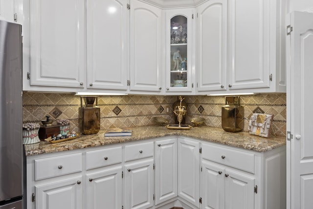 kitchen with tasteful backsplash, stainless steel refrigerator, white cabinetry, and light stone counters