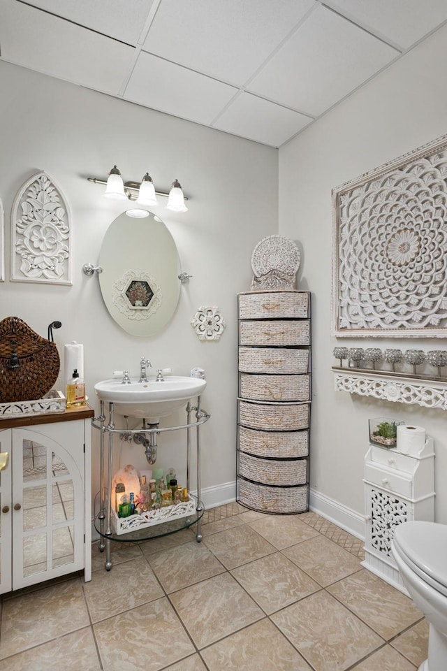 bathroom with tile patterned flooring, a drop ceiling, and toilet