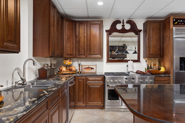 kitchen featuring a drop ceiling, dark stone countertops, high quality appliances, and sink