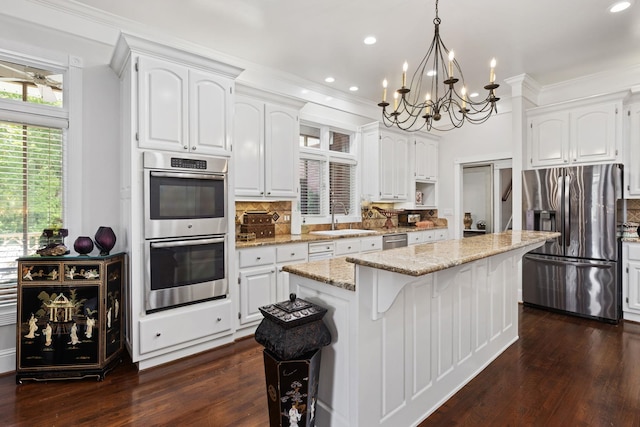 kitchen featuring a center island, backsplash, white cabinets, hanging light fixtures, and appliances with stainless steel finishes