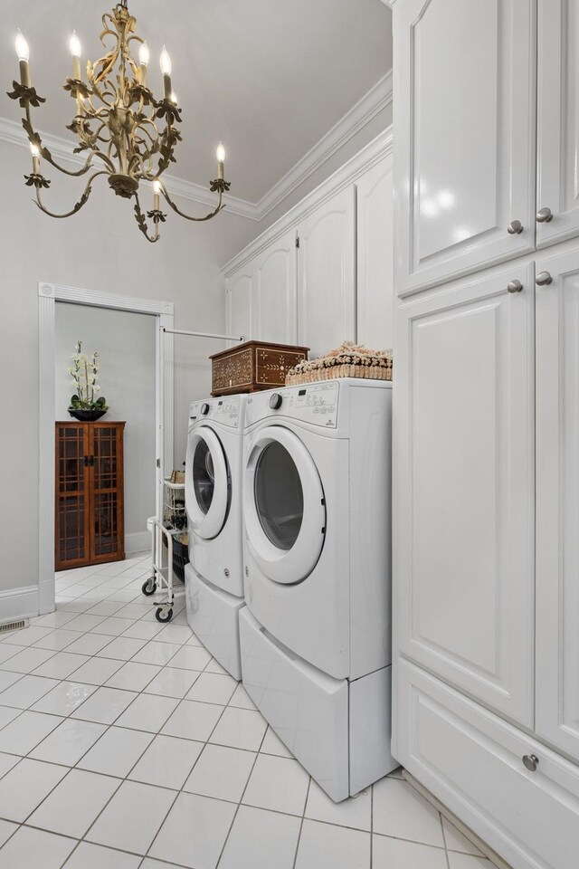 clothes washing area featuring washing machine and clothes dryer, cabinets, an inviting chandelier, light tile patterned flooring, and ornamental molding