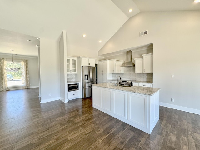 kitchen with white cabinets, wall chimney exhaust hood, decorative backsplash, an island with sink, and stainless steel fridge with ice dispenser