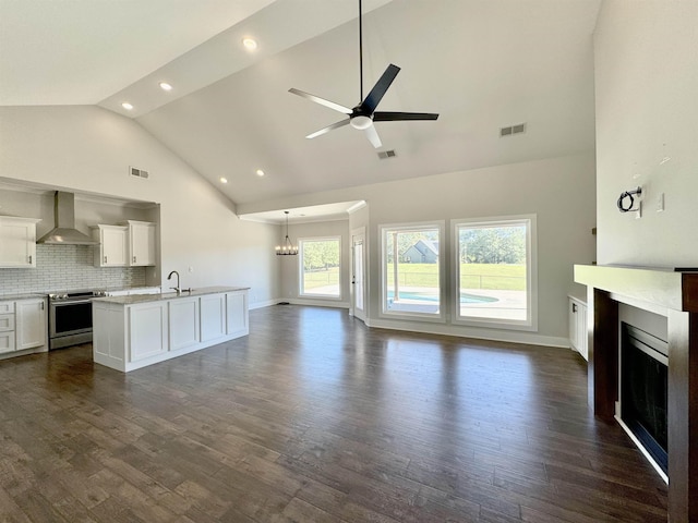 kitchen featuring a kitchen island with sink, wall chimney range hood, sink, stainless steel stove, and white cabinetry