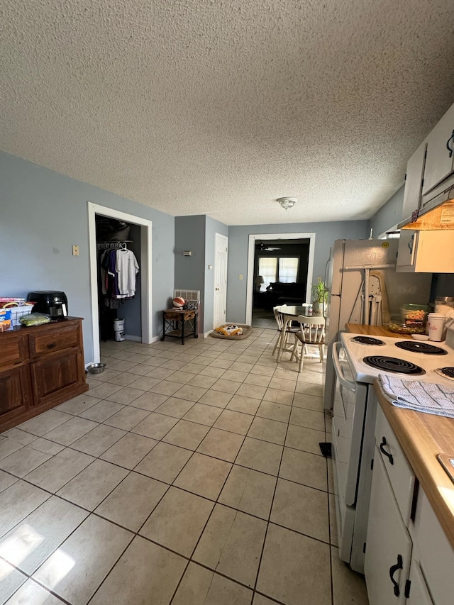 kitchen featuring white cabinets, a textured ceiling, white range with electric stovetop, and light tile patterned flooring