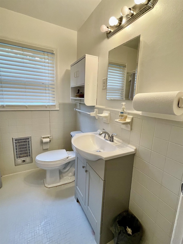 bathroom with tile walls, heating unit, a wainscoted wall, vanity, and toilet