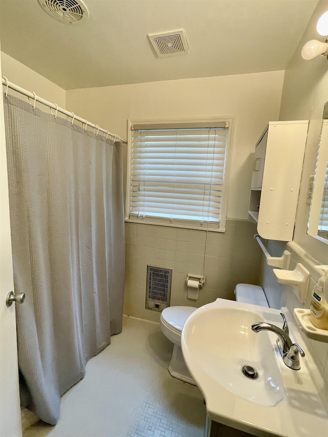bathroom featuring heating unit, a sink, toilet, tile walls, and a wainscoted wall