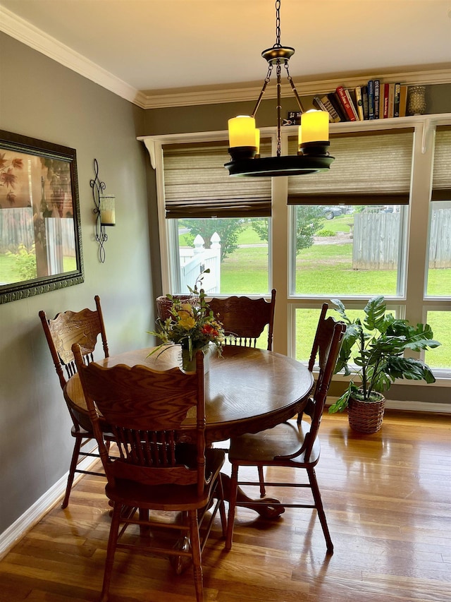 dining area featuring healthy amount of natural light, crown molding, baseboards, wood finished floors, and a chandelier