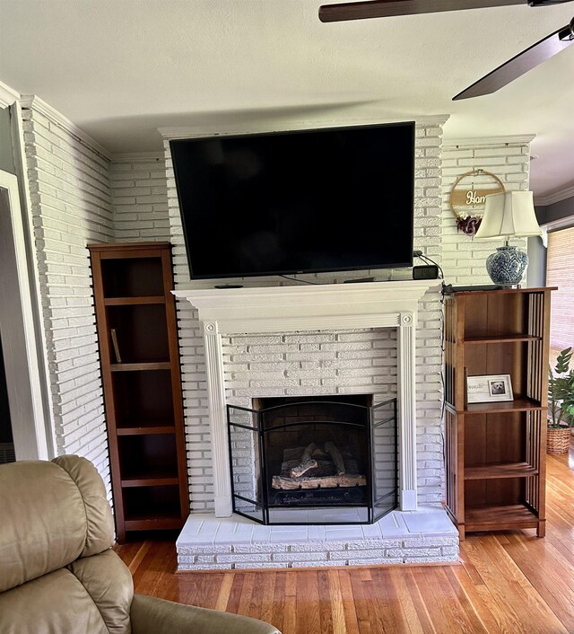 living room with ornamental molding, a fireplace, a ceiling fan, wood finished floors, and brick wall