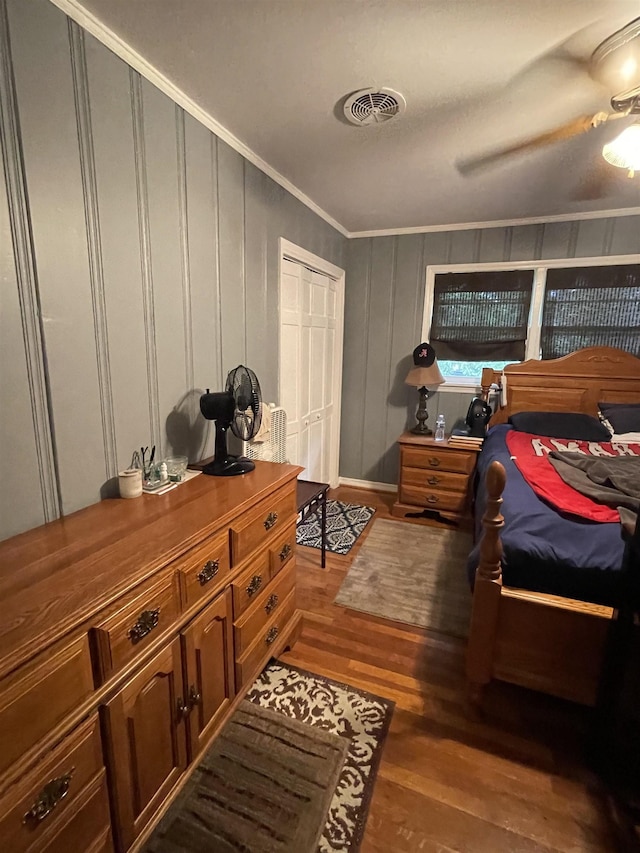 bedroom with wood finished floors, ornamental molding, ceiling fan, and a decorative wall