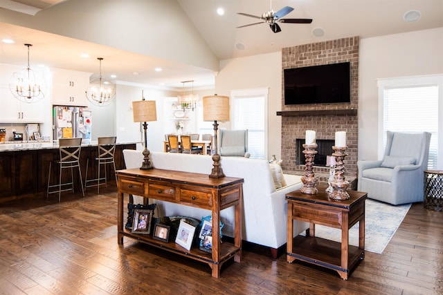 living room with a brick fireplace, ceiling fan with notable chandelier, and dark wood-type flooring