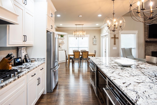 kitchen with appliances with stainless steel finishes, premium range hood, light stone countertops, white cabinets, and decorative light fixtures