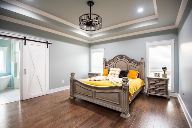 bedroom with ornamental molding, a tray ceiling, a barn door, dark wood-type flooring, and ensuite bath