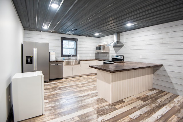 kitchen featuring wall chimney range hood, sink, light hardwood / wood-style flooring, stainless steel appliances, and kitchen peninsula