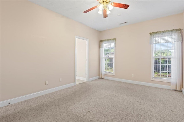empty room with light colored carpet, a ceiling fan, and baseboards