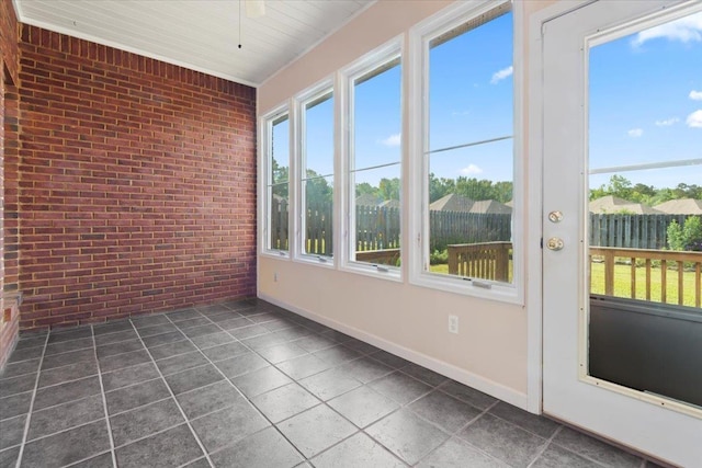 unfurnished sunroom featuring brick wall, tile patterned floors, and baseboards